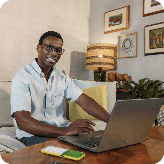 Homem preto utiliza notebook com celular ao lado exibindo o app PagBank, representando a comodidade da pré-autorização de pagamentos.