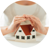 Mãos sobre a maquete de uma casa branca, com janelas verdes e telhado vermelho.