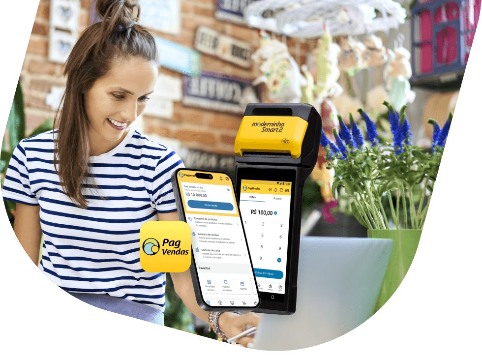 Mulher branca, de cabelos castanhos e expressão sorridente em sua loja de plantas. Ela está vestindo uma camiseta de manga curta com listras azuis. Sobre a imagem temos um celular com o aplicativo do PagVendas aberto e uma maquininha modelo Moderninha Smart 2 mostrando a tela de cobrar venda.