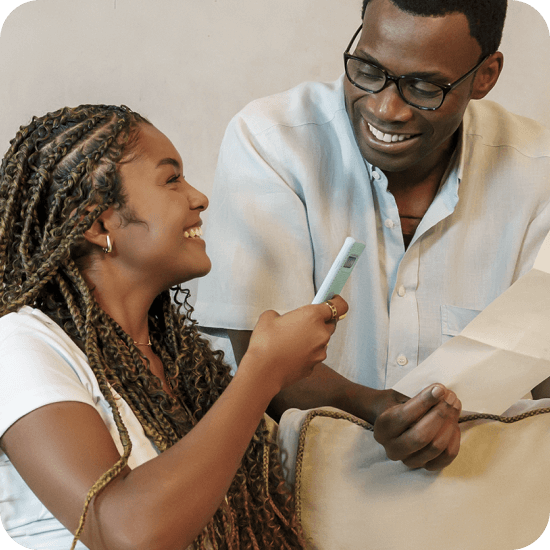 Mulher preta com celular azul e homem preto com papel interagem de forma leve, representando organização e praticidade no agendamento de contas e boletos pelo PagBank.
