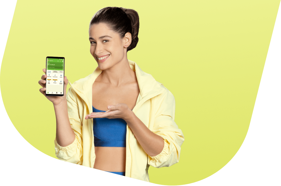 Atriz Luiza Arraes, mulher branca, de cabelo preto e expressão sorridente. Ela está usando um top azul com uma camisa amarela aberta por cima e segurando um celular com o aplicativo PagBank aberto.