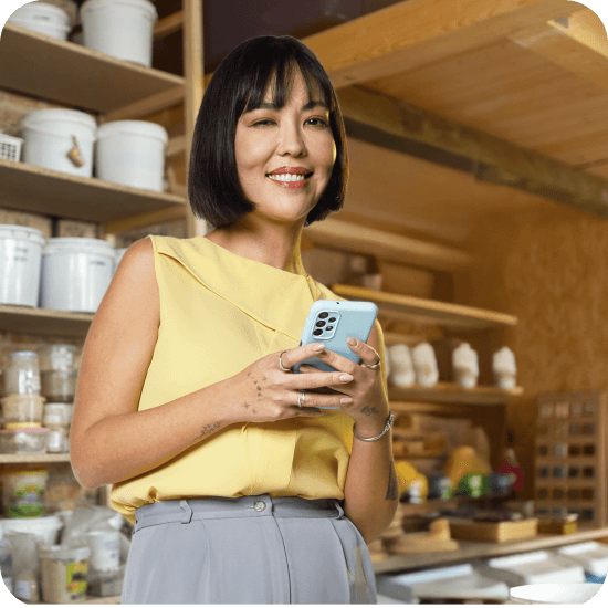Mulher asiática segura um celular azul, representando o uso do Poupar Automático do PagBank para guardar parte das vendas e fazer o dinheiro render.