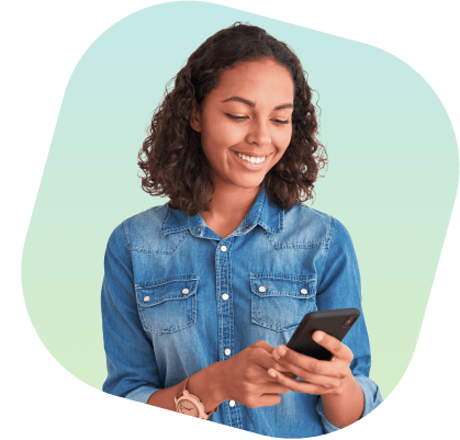 Mulher negra, de cabelo castanho e expressão sorridente. Ela está usando uma camisa jeans de manga longa dobrada e um relógio marrom, segurando um celular.