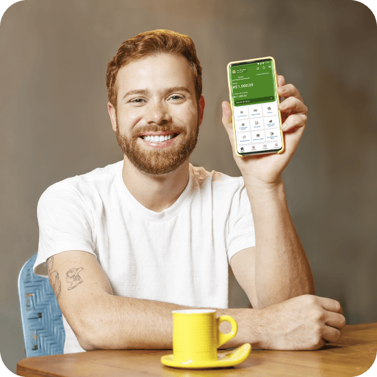 Homem branco sorridente segura um celular com o app do PagBank aberto, transmitindo praticidade e controle ao trazer o salário para o PagBank.
