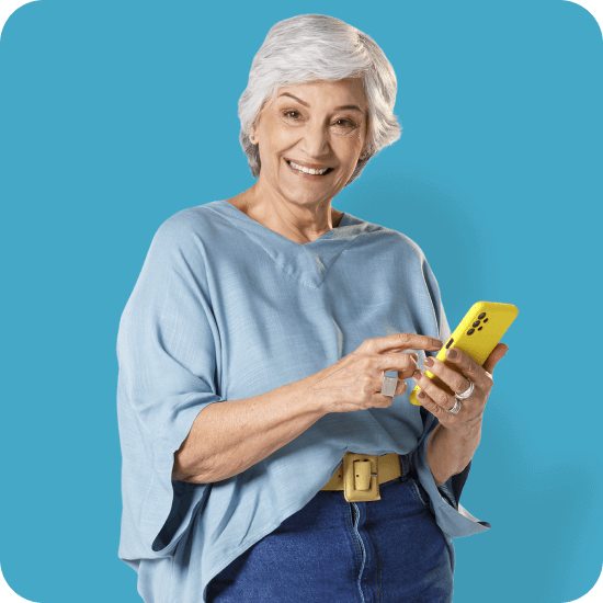 Mulher idosa segura um celular amarelo com o app PagBank aberto, simbolizando facilidade para investir com carteiras recomendadas, autonomia financeira e praticidade pelo aplicativo.