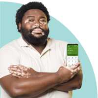 Homem preto com vitiligo segura um celular com o app PagBank aberto, representando acesso às notícias do mercado financeiro e dicas de investimento pelo grupo exclusivo no Telegram.