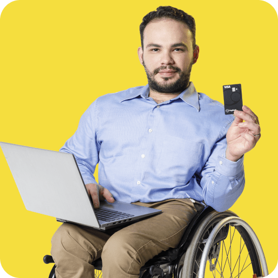 Homem branco cadeirante segura um cartão PagBank com um notebook aberto no colo, representando inclusão, autonomia e praticidade ao usar um cartão sem anuidade em um banco digital completo.